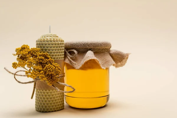Tarro con miel cerca de vela hecha a mano sobre fondo beige - foto de stock