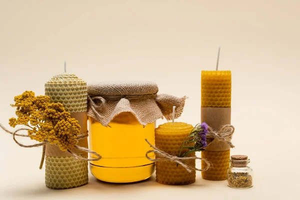 Craft candles with dry flowers and jar with honey on beige background — Stock Photo