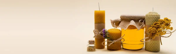 Bougies artisanales avec des fleurs près du pot avec du miel sur fond beige, bannière — Photo de stock