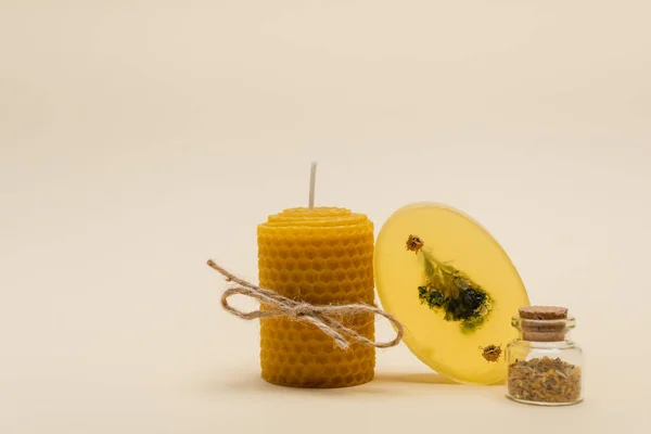 Vela casera con cordel cerca de la barra de jabón y frasco con hierbas sobre fondo beige - foto de stock