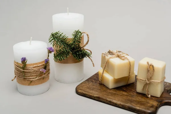 Bougies avec plantes et barres de savon sur planche à découper sur fond gris — Photo de stock