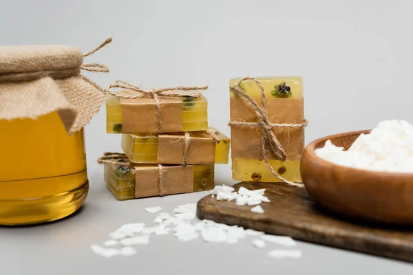 Handmade soap near blurred wax and jar with honey on cutting board on grey background — Stock Photo