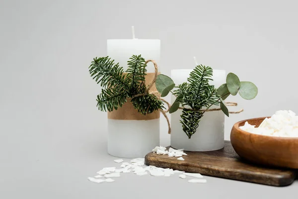 Beeswax flakes near handmade candles with plants on grey background — Stock Photo