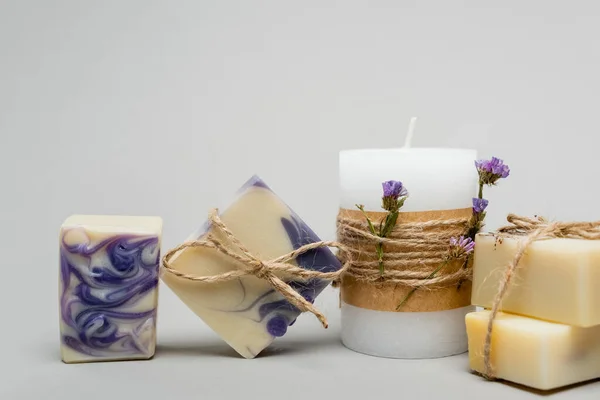 Handmade soap near candle with flowers on grey background — Stock Photo