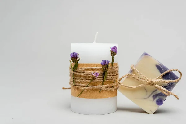 Handgemachte Seifenstange mit Bindfaden bei Kerze mit Blumen auf grauem Hintergrund — Stockfoto