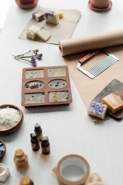 Barras de jabón en molde de silicona cerca de cortador, papel artesanal y aceites esenciales en la mesa - foto de stock