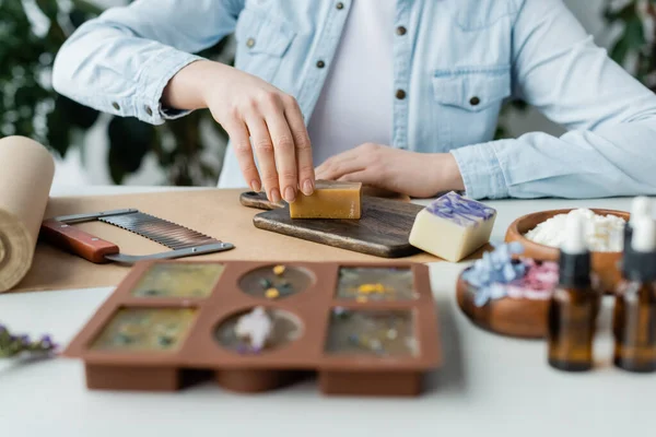 Vista ritagliata di artigiana in possesso di sapone sul tagliere e carta artigianale a casa — Foto stock