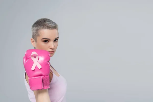 Jolie femme montrant gant de boxe rose avec ruban de sensibilisation au cancer du sein isolé sur gris — Photo de stock