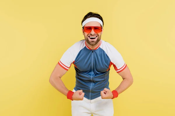 Cheerful sportsman showing muscles isolated on yellow — Stock Photo