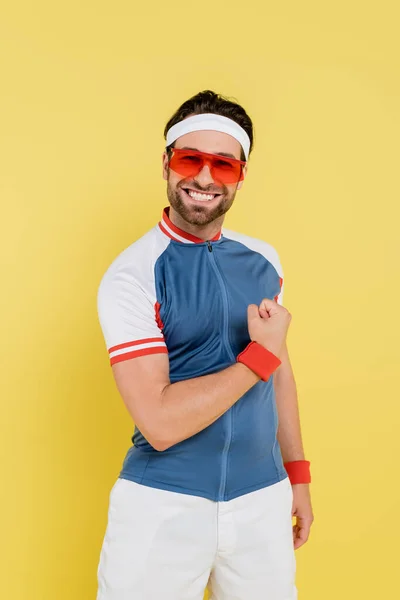 Positive sportsman in sunglasses showing muscles isolated on yellow — Stock Photo