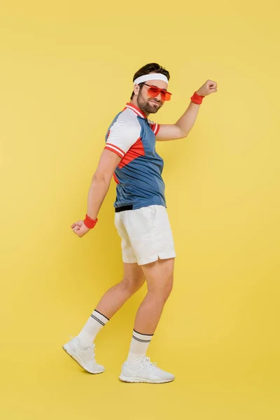 Full length of young sportsman showing muscles on yellow background — Stock Photo