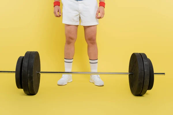 Cropped view of barbell near sportsman standing on yellow background — Stock Photo