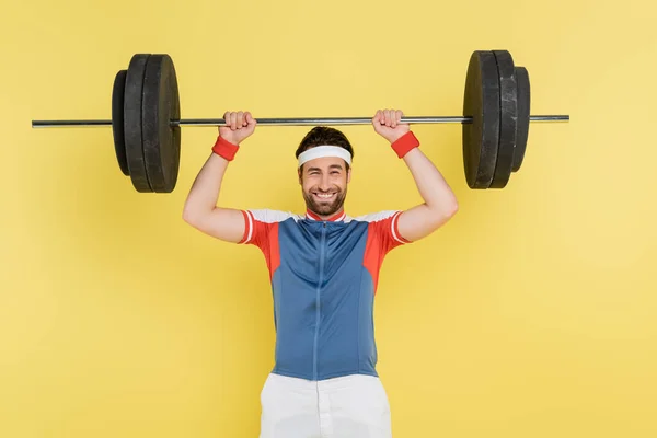 Esportista positivo levantando barbell isolado em amarelo — Fotografia de Stock