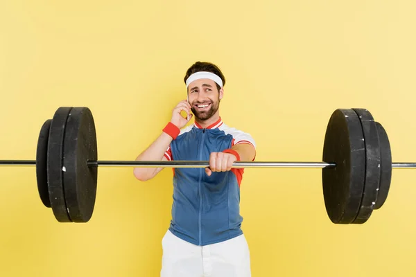 Sportivo sorridente che parla su smartphone e tiene isolato il bilanciere su giallo — Foto stock