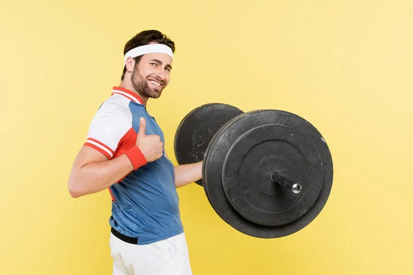 Deportista sonriente mostrando como gesto y levantando la barra aislada en amarillo - foto de stock