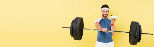 Sportif positif tenant savoureux gâteau et haltère isolé sur jaune, bannière — Photo de stock