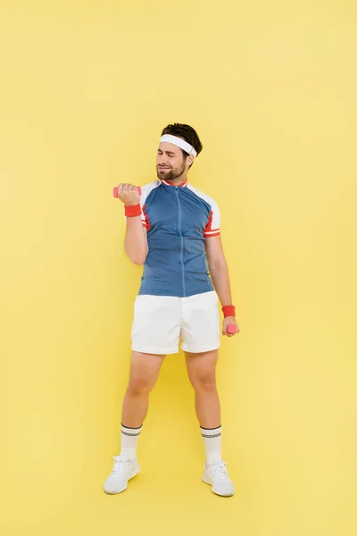 Full length of smiling sportsman working out with dumbbells on yellow background — Stock Photo