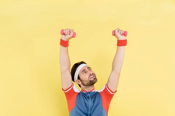 Brünetter Sportler hebt Hanteln und blickt isoliert auf gelb — Stockfoto