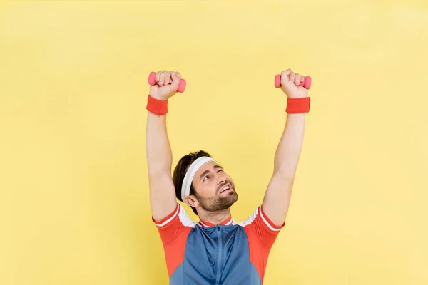 Morena desportista levantando halteres e olhando para cima isolado no amarelo — Fotografia de Stock