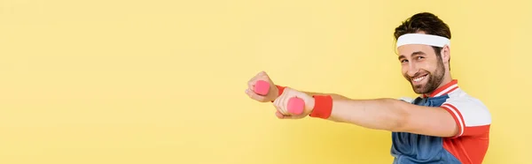 Deportista sonriente mirando a la cámara mientras entrena con mancuernas aisladas en amarillo, pancarta - foto de stock