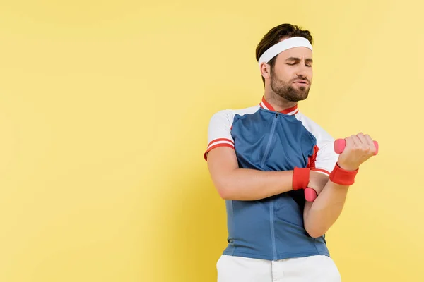 Напряжённый спортсмен работает с гантелями, изолированными на жёлтом — стоковое фото
