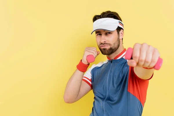 Giovane sportivo in visiera che lavora con manubri isolati sul giallo — Foto stock