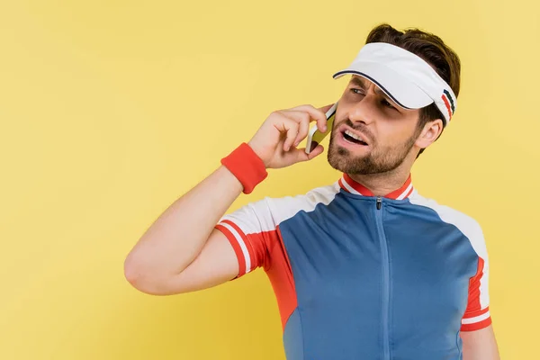 Angry sportsman in visor talking on mobile phone isolated on yellow — Stock Photo