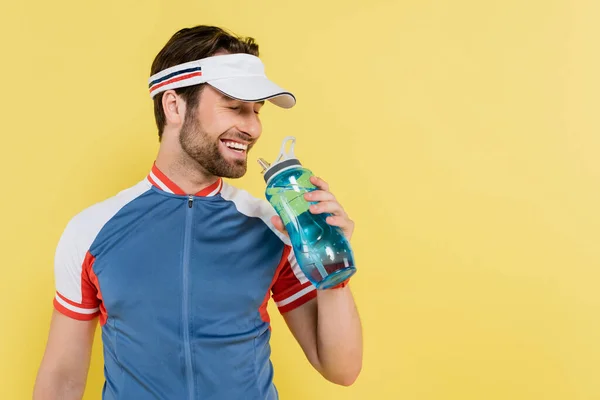 Smiling sportsman in visor holding sports bottle isolated on yellow — Stock Photo