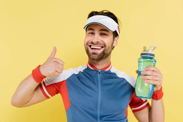 Deportista sosteniendo botella deportiva y mostrando como gesto aislado en amarillo - foto de stock