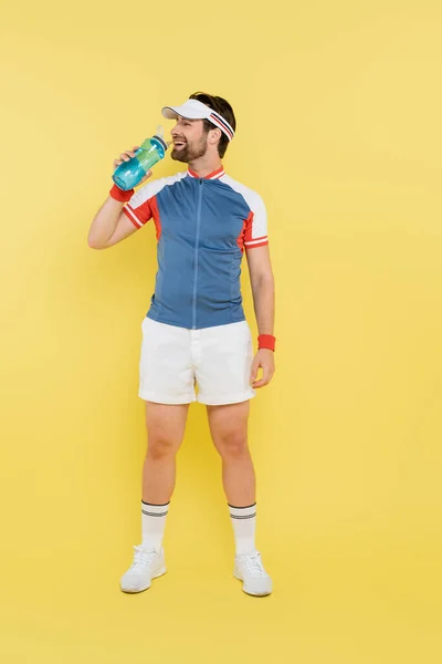 Longitud completa de deportista sonriente sosteniendo botella deportiva sobre fondo amarillo - foto de stock