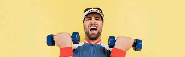 Vista de bajo ángulo del joven deportista haciendo ejercicio con mancuernas aisladas en amarillo, pancarta - foto de stock