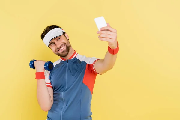 Allegro sportivo che si fa selfie mentre si allena con i manubri isolati sul giallo — Stock Photo