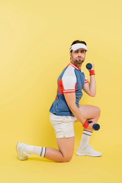 Allenamento sportivo barbuto con manubri e guardando lontano su sfondo giallo — Foto stock