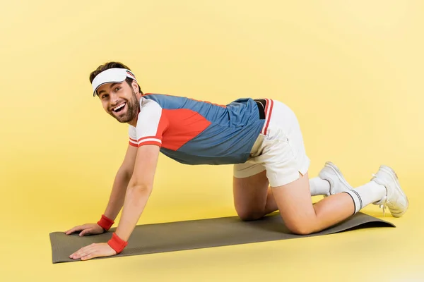 Deportista positivo de pie en la alfombra de fitness sobre fondo amarillo - foto de stock