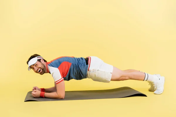 Deportista positivo parado en la tabla en la estera de la aptitud sobre fondo amarillo - foto de stock