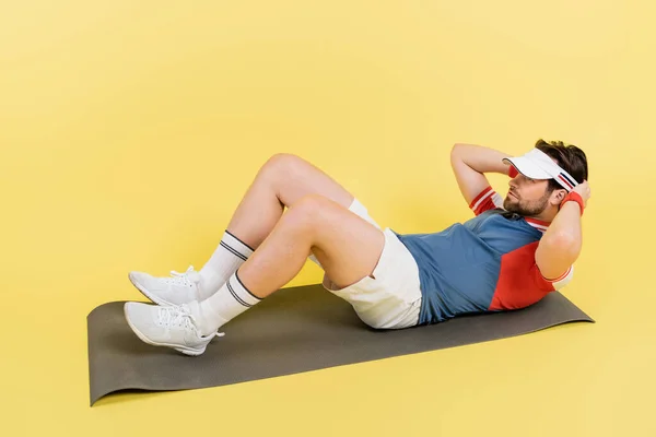 Deportista barbudo haciendo abdominales en la alfombra de fitness sobre fondo amarillo - foto de stock