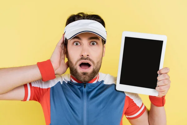 Шокированный спортсмен держит цифровой планшет с чистым экраном, изолированным на желтом — стоковое фото