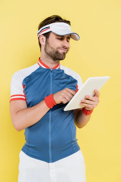 Deportista escéptico usando tableta digital aislada en amarillo - foto de stock