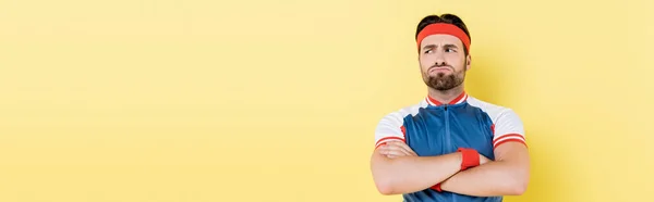 Pensive sportsman crossing arms and looking away isolated on yellow, banner — Stock Photo