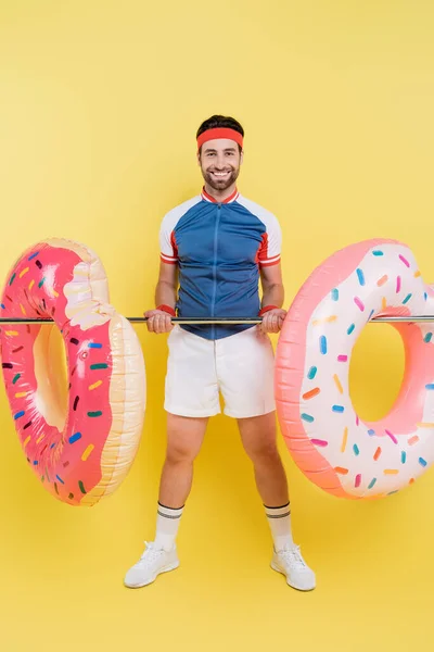 Full length of cheerful sportsman holding swim rings on pipe on yellow background — Stock Photo