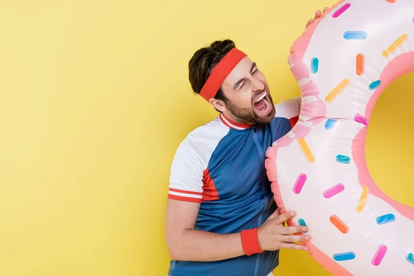 Young sportsman opening mouth while holding swim ring isolated on yellow — Stock Photo