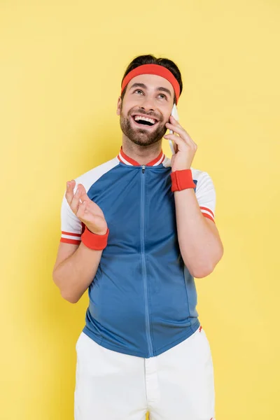 Positive sportsman talking on smartphone isolated on yellow — Stock Photo