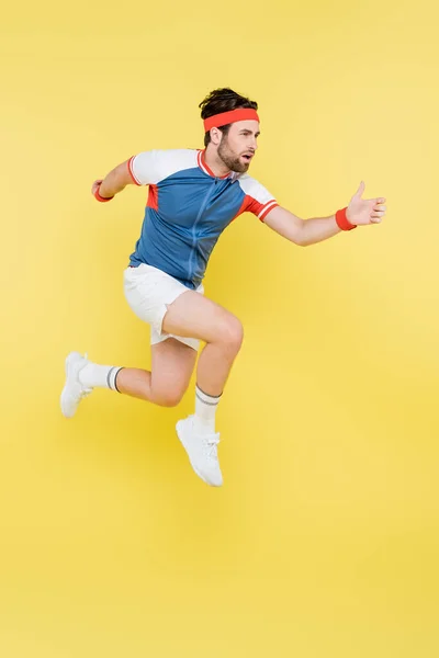 Bearded sportsman jumping and looking away isolated on yellow — Stock Photo