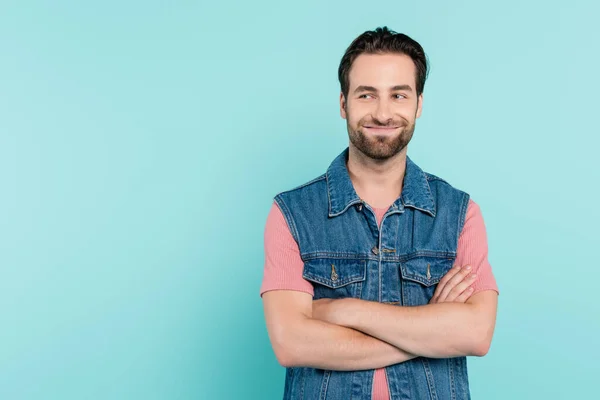 Uomo sorridente in gilet di denim incrocio braccia isolato su blu — Foto stock