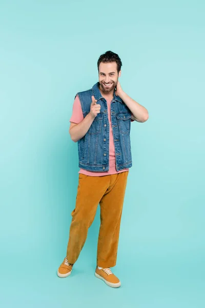 Full length of positive man pointing at camera on blue background — Stock Photo