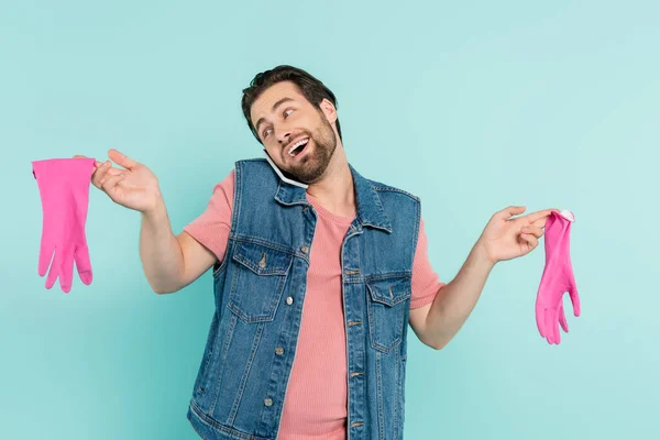 Uomo positivo in possesso di guanti di gomma e parlando su smartphone isolato su blu — Foto stock