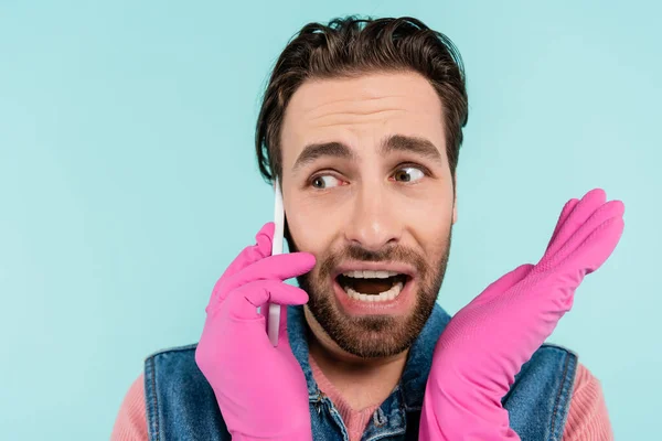 Jeune homme en gants de caoutchouc parlant sur téléphone portable isolé sur bleu — Photo de stock