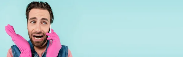 Brunette homme en gants de caoutchouc parlant sur smartphone isolé sur bleu, bannière — Photo de stock