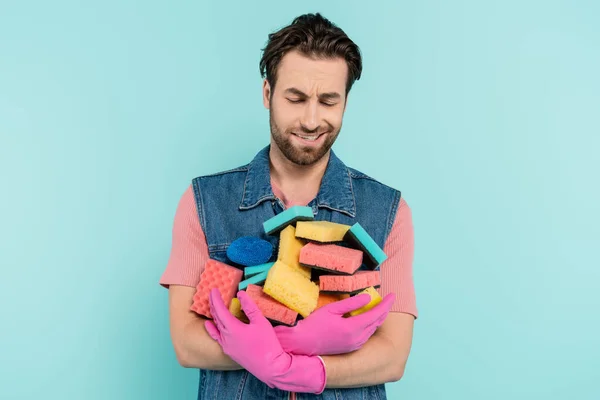 Displeased unmarried man in rubber gloves holding sponges isolated on blue — Stock Photo
