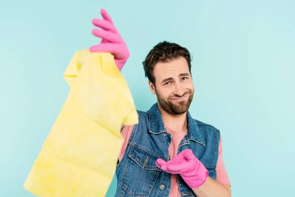 Lächelnder Mann in Gummihandschuhen zeigt auf verschwommenen Teppich auf blauem Grund — Stockfoto